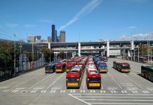 Metro Adding Hydrogen Buses, Auditor Casts Doubt on Fleet Electrification Strategy Rows of buses with the I-90 ramps and Seattle skyscrapers in the background.