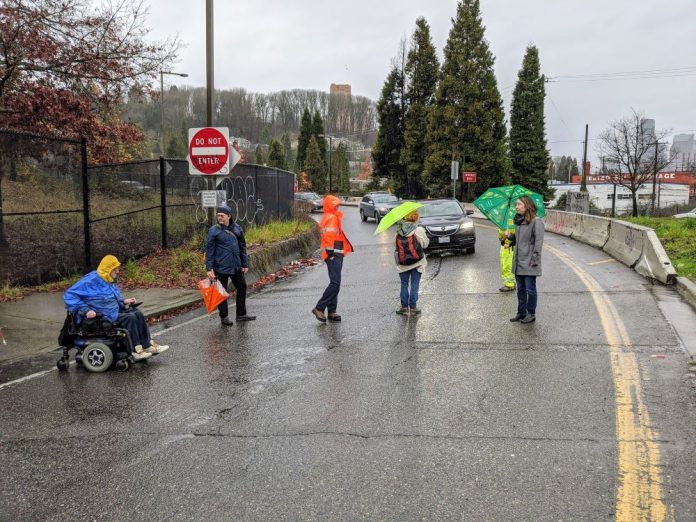 People walk and roll across the street in the rain with a car in the background."This system is broken for us already. We want change. We want a different and a re-imagined transportation system," was the caption I wrote for my presentation. (Photo by David Seater)