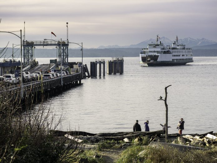 Folks walk the beach as the Washington State ferry comes in. Cars wait on the dock.