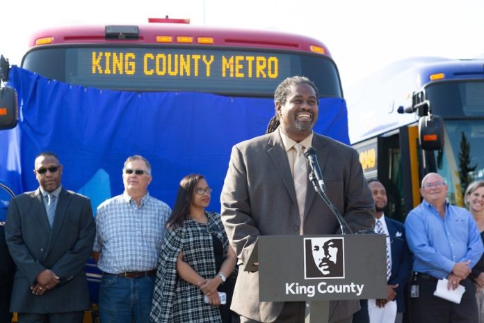Terry White - King County Metro Terry White at a podium in front of a Metro bus flanked by Metro coworkers at a 2018 event.