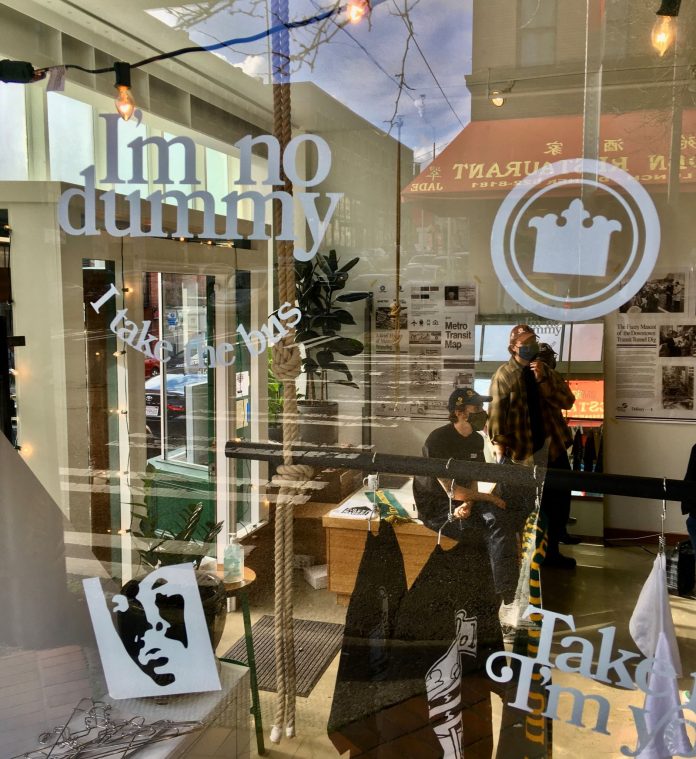 Chinatown street reflects in the window of the popup store where Nate and Ryan lean on a counter near their merch.