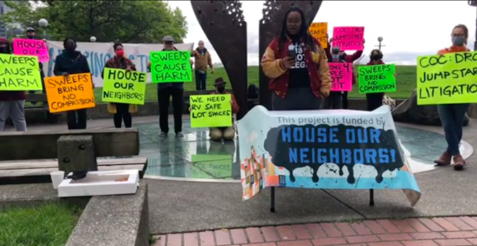 Screen Shot 2021-05-19 at 3.08.41 PM A photograph showing participants holding colorful signs at a press event. The signs carry messages such as "sweeps cause harm" and "sweeps bring no compassion"
