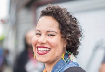 Nikkita Oliver 2021 Questionnaire – Seattle City Council Pos. 9 Nikkita is a Black woman. She wears rainbow hoop earrings. her curly hair to the side, and a big smile.