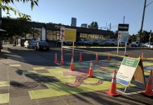 Seattle’s Neighborhood Recovery Fund Open for Proposals A photograph of a parking lot that has been painted with a brightly colored mural. Traffic cones mark the area surrounding part of the mural, and an A frame sign reads "pavement to parks."