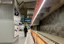A Peek Inside the U District Link Light Rail Station A photo of an underground light rail station platform. A man walks away from the camera. The train tracks are empty.