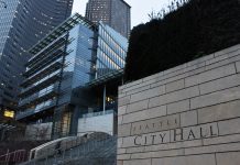 Op-Ed: Lowering Ethical Standards to Allow Elected Officials’ Self-Dealing is a Terrible Idea A photo of the Seattle City Hall with tall glass buildings illuminated at dusk in the background.