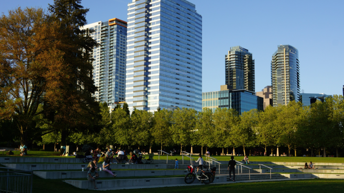 08-downtown-park A photo of amphitheater style seating in a park with people sitting in the grass and tall modern buildings in the backdrop.