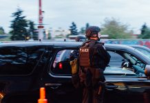 How to Reduce SPD’s Budget, Improve Public Safety A photo shows a police officer in riot gear standing next to a patrol car.