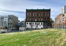 Former Battery Tunnel Site Gets Green Light for Downtown School A photo of a green field with a chainlink fence and brick building with a white mural in the background.