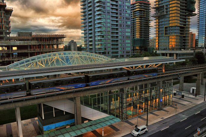 metrotown station bc aagay creative commons A photo of a light rail station surrounded by tall modern buildings, some of which are still under construction.