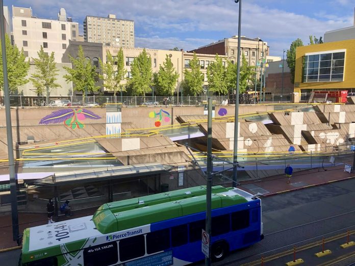 17603076-7297-4A54-906B-CEA9FFF37DE8_1_201_a A photo shows a bus in front a public art water feature with brightly colored images painted on cement.