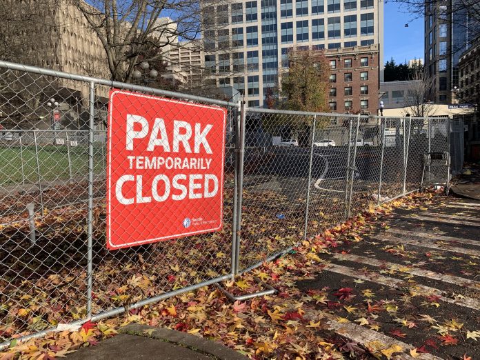City-Hall-park-closed A photo of a chainlink fence and a sign reading "park closed" in front a open grassy area.