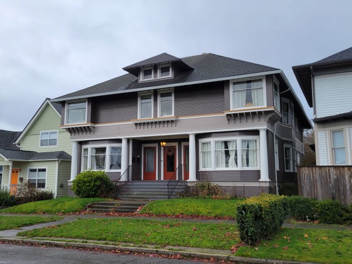 Tacoma triplex A photo of a grey triplex with red doors that maintains the scale of a large single family house.