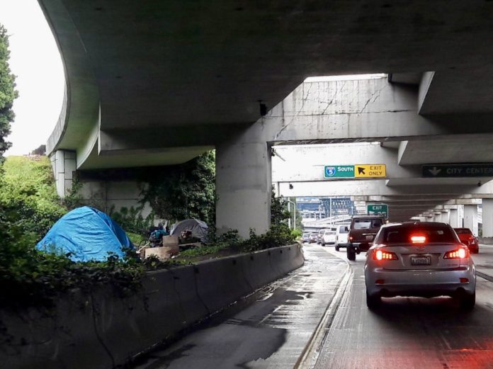 B69BB4F3-417B-4D03-A78A-4F0ACDE4D4EA_1_201_a a photo of a freeway with cars and a tent behind a concrete barrier.