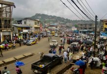 Latest IPCC Climate Report Underscores Need for Collaborative Action Among Urbanists A photo of a dirt street crowded with people and vehicles with a green mountain in the distance and electrical wire