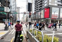 Elected Leaders Shy Away From Big Amendments to 2050 Regional Transportation Plan A bike rider waits at a busy intersection in downtown Seattle as pedestrians cross