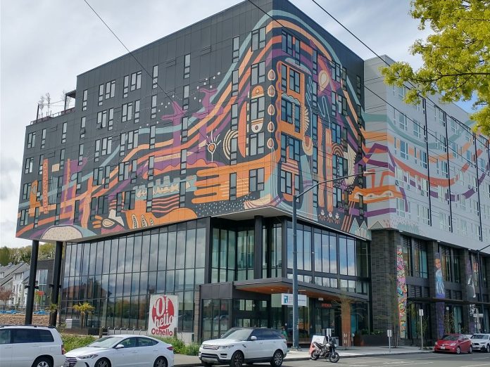 A gray and white midrise building with an orange art wrap.
