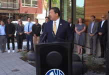 Seattle Leaders Eye JumpStart Housing Funds to Close $230 Million Budget Hole Bruce Harrell wears a suit and stands at a podium with a group of people standing behind him.