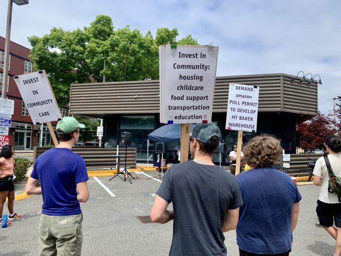 9BE89F39-397A-4385-877E-C0B95AE13758_1_201_a people stand in a parking lot holding stands calling for more community investment