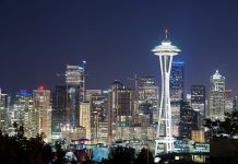 The Urbanist Podcast: Your Guide to City Ranking Lists Illuminated Space Needle in front of a city of lit windows with a darkening sky.