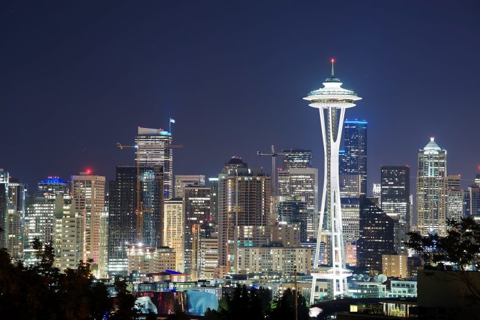 Illuminated Space Needle in front of a city of lit windows with a darkening sky.