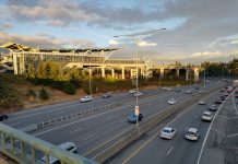 Tukwila Gets Serious about Transit-Oriented Housing The elevated station gleams as the sun is going down over a busy freeway trench.