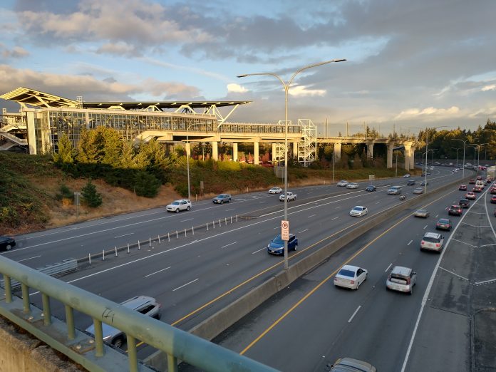 The elevated station gleams as the sun is going down over a busy freeway trench.