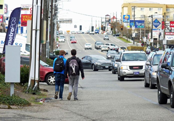 Aurora Avenue in North Seattle Rows of cars on a block of drive thrus and strip malls as two kids walk in the gutter of the road.