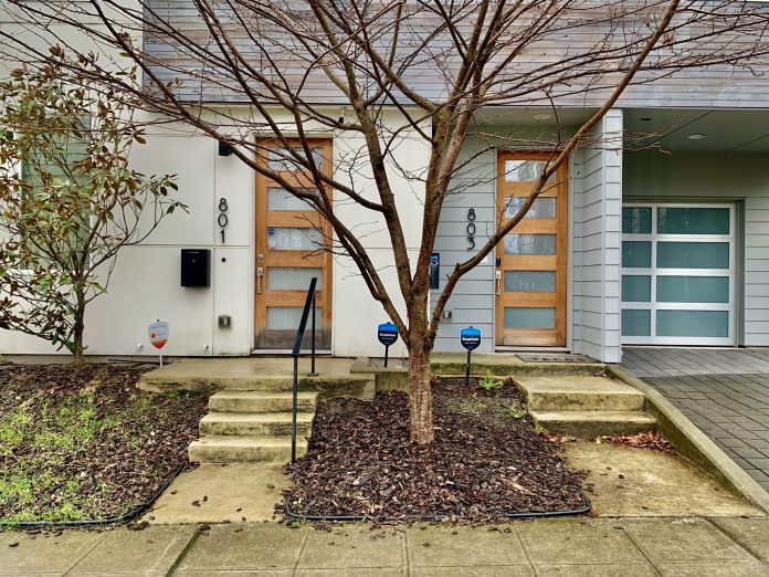 Duplex missing middle houising two doors with addresses with a tree in the center and drive with garage in back