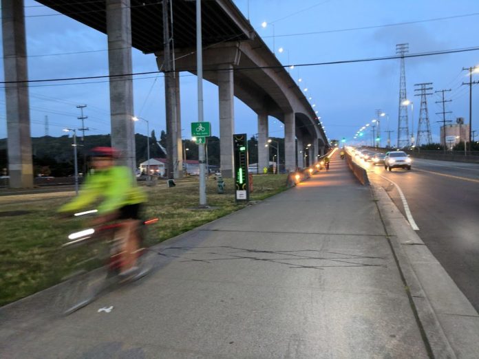 The low bridge stands at dusk with the high bridge above it, and a cyclist is coming off the bridge and is blurred by motion