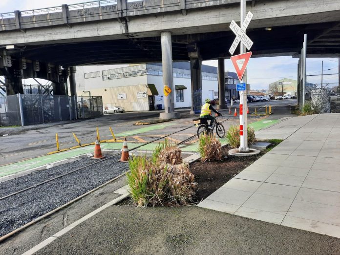 Railroad crossing sign with cyclist A railroad crossing sign marks the spot next to some shrubs.