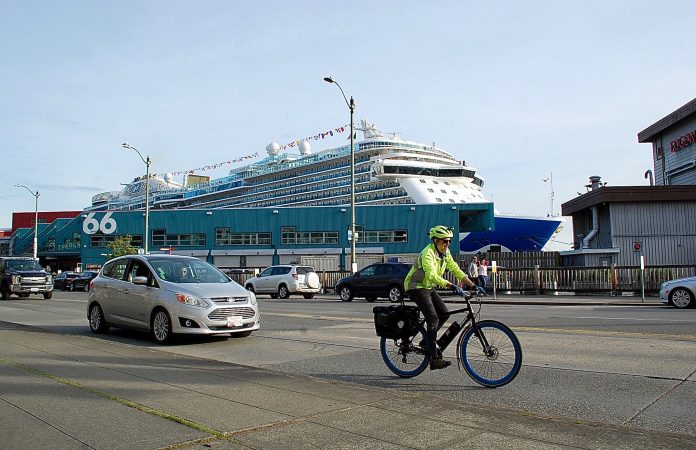 cruise ship and cyclist andrew engelson 05-23 Bicyclist in neon jacket and helmet on busy street. Cruise terminal and ship behind him.