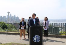 Op-Ed: Harrell Seeks to Derail Social Housing with Deceptive Campaign Mailer Bruce Harrell in a suit standing at a lectern. MLK Labor’s Executive Secretary-Treasurer Katie Garrow is to the left and OSE Director Jessyn Farrell to the right. A hazy Seattle skyline is in the background from Queen Anne vantage.