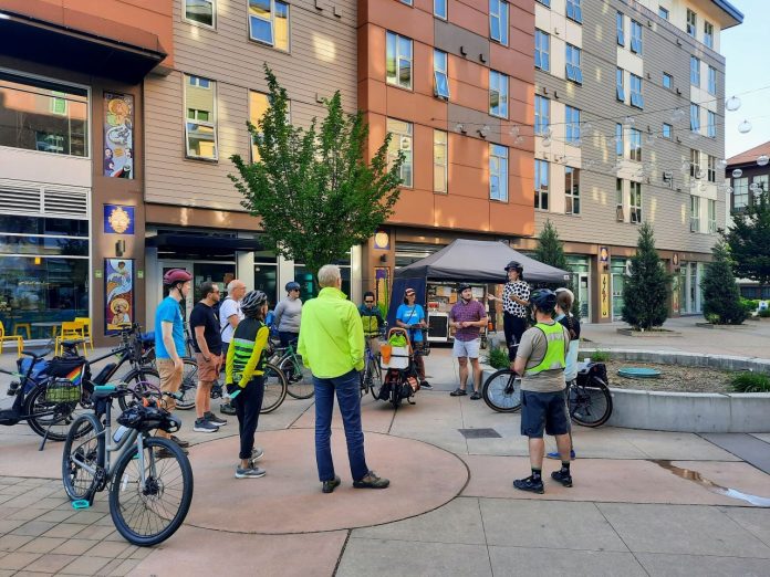 A dozen people gather in the courtyard plaza between the buildings that compose El Centro de La Raza complex.