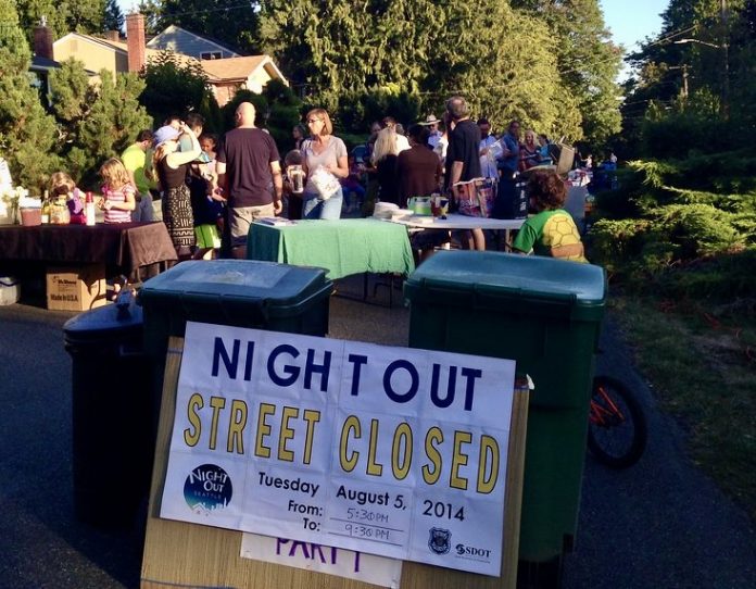 14864767643_5fb2a9b232_b A sign reads Night Out street closed with people gathered behind it socializing.