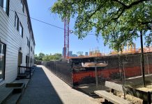 Black History and Ambition Meet at an Expanding Bryant Manor Existing housing separated by a sidewalk from a large construction site with crane.