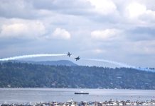 Op-Ed: It’s Time for Seattle to Cancel the Blue Angels Two Navy Blue Angels planes pass each other over boats tied to a log boom in Lake Washington.