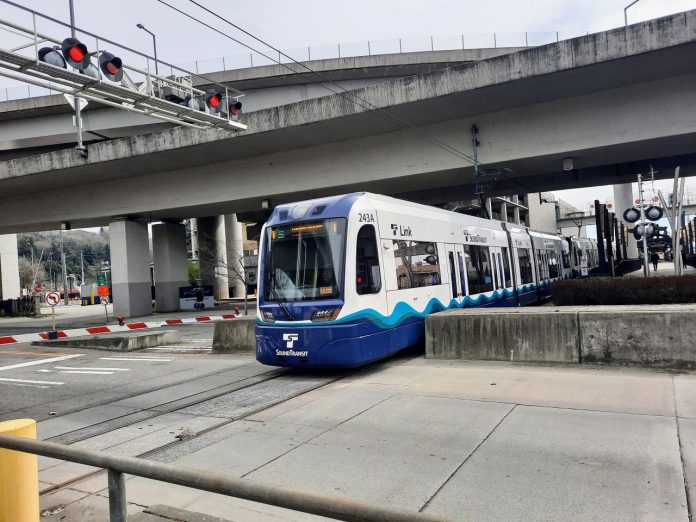 Link-train-in-SoDo-rail-crossing-by-Doug-Trumm A light rail train in SoDo passes under highway overpasses and enters an intersection.