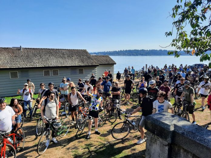CityNerd-Urbanist-bike-riders-waiting-to-embark-from-Mount-Baker-Beach-20230916_110339 A crowd of more than 100 bicyclists assembled with Lake Washington in the background.