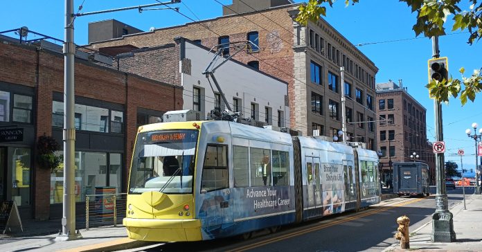 Yellow front of a streetcar passing in front of brick buildings.