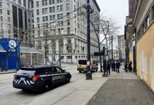 Harrell Cuts Social Safety Net to Fund 16% Boost to SPD A half dozen police and a medic team talk to a person in a wheel chair across from Pioneer Square Station. A police cruiser and ambulance are parked along Third Avenue.