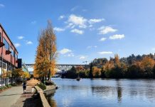 2023 Year-End Update and Fundraising Push People jog and walk along the Burke-Gilman Trail along the canal in Fremont, with a tug boat chuggling along and the bascule bridge and steel high bridge in the background.
