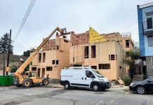 Seattle’s Housing Construction Booms While Permitting Flashes Warning Signs A small crane move materials to the top of a three story townhome complex where a construction work receives them.