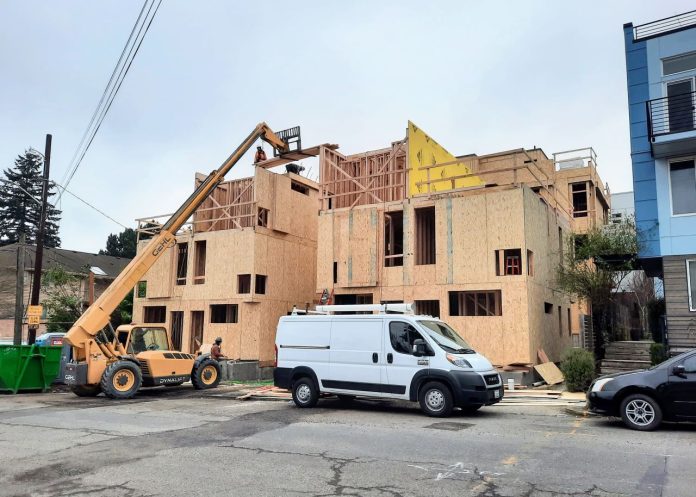Townhome construction on Woodland Park Avenue 20230124 A small crane move materials to the top of a three story townhome complex where a construction work receives them.