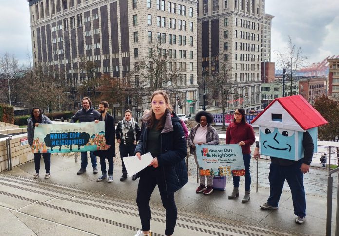 Social housing advocates stand on the steps of Seattle City Hall with their house mascot.