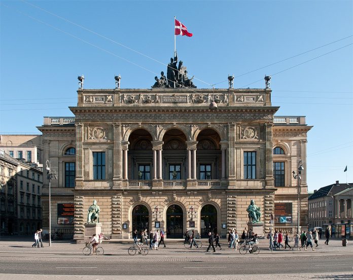 Royal_Danish_Theatre_Copenhagen_by_AxelKuhlmann Two greenish copper statues frank the entrance to the theater, which flies a Danish flag at its apex.