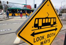 New Energy for Changes on MLK Corridor, But Few New Ideas A look both ways yellow sign includes a light rail symbol. Pedestrian wait at the opposite corners of MLK Way.