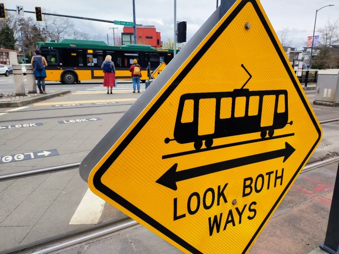 MLK Sign A look both ways yellow sign includes a light rail symbol. Pedestrian wait at the opposite corners of MLK Way.