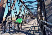 Washington’s E-bike Rebate Program Launches Wednesday A person bikes on a trestle bridge with a few pedestrians in the background.