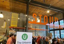 Join The Urbanist for Our Monthly Meetup Tonight An Urbanist banner standing in a corner of a brewery with a few dozen people gathered chatting.